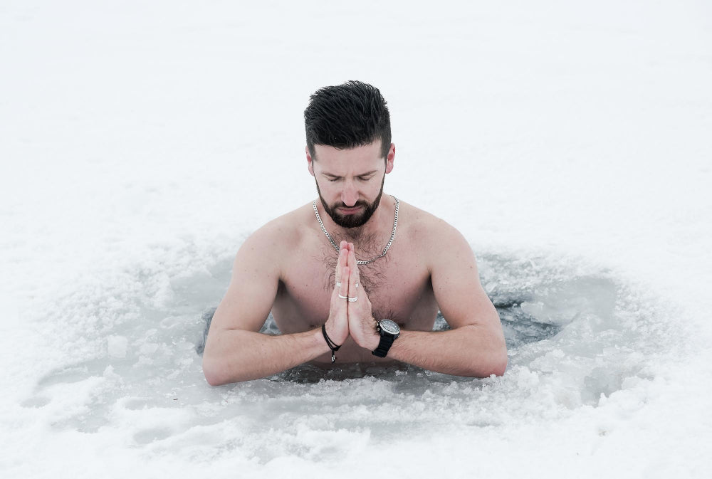 A man meditates in an ice hole in a snowy environment, hands in prayer position, displaying focus and tranquility.